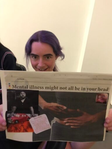 Student at the art workshop holding up their art. A student with long purple hair tied up. 